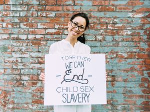 A Girl holding a sign that reads "Together we can end child sex slavery"