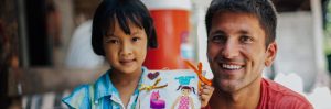 A man and a girls smiling while she holds up a picture she made.