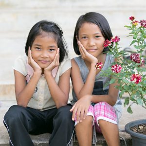 Two smiling girls next to some flowers.