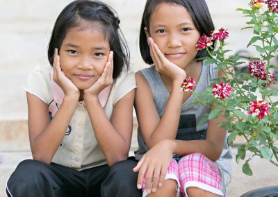 Two smiling girls next to some flowers.