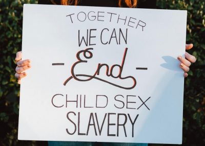 A girl holding a sign that reads "Together We Can End Child Sex Slavery"